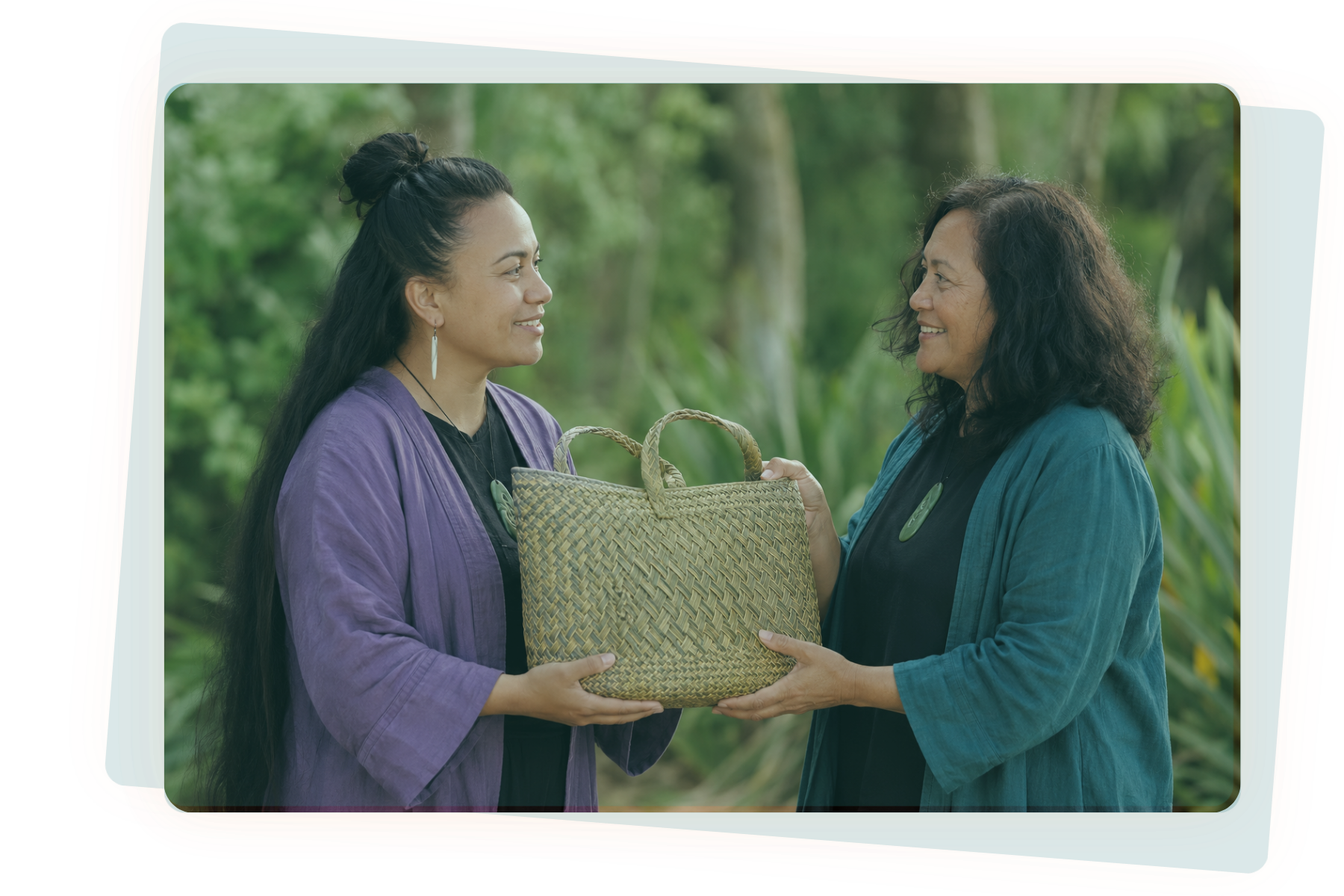 Two Māori women handing each other a kete, smiling